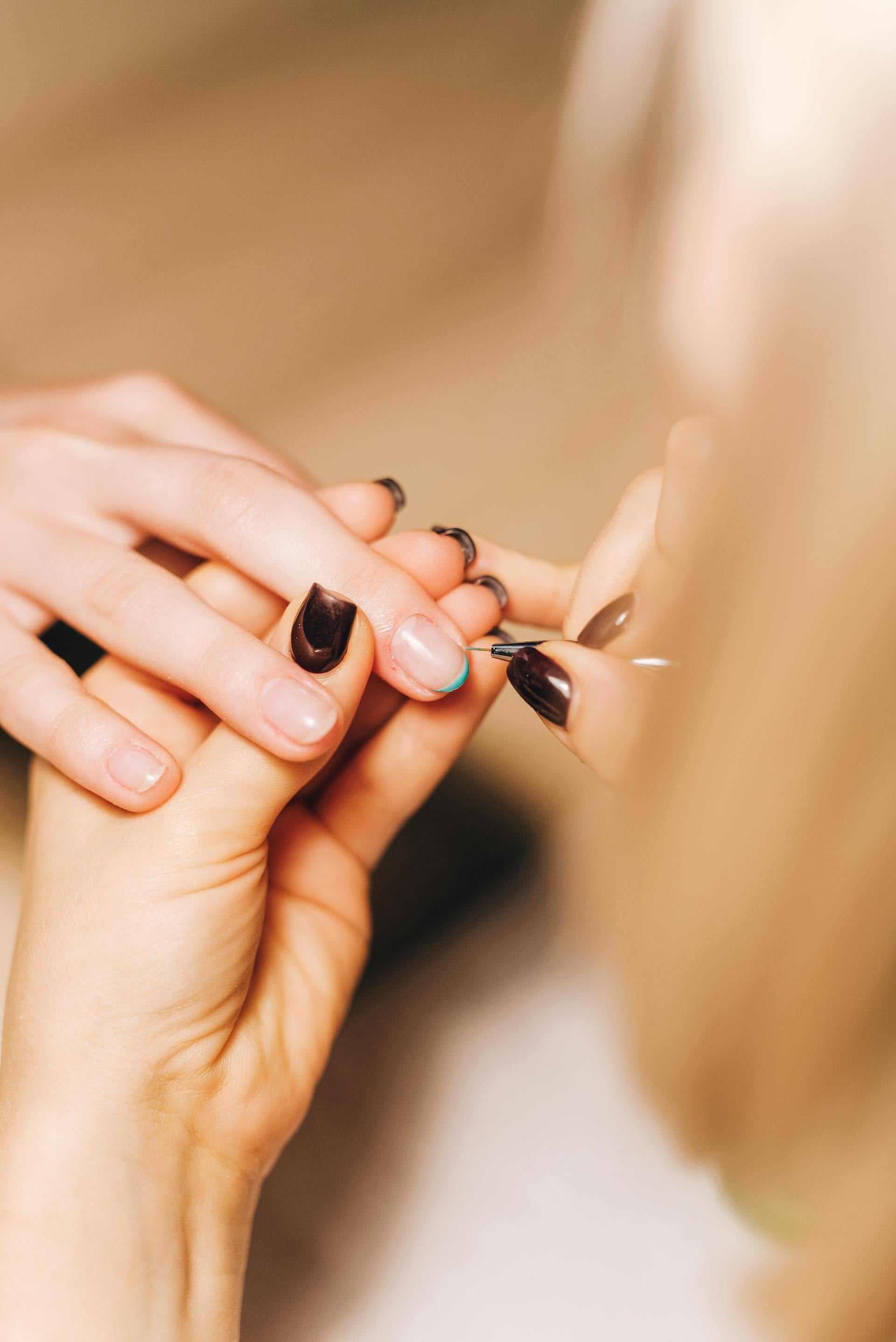 Manicure process with nail art being applied to client's fingernail.