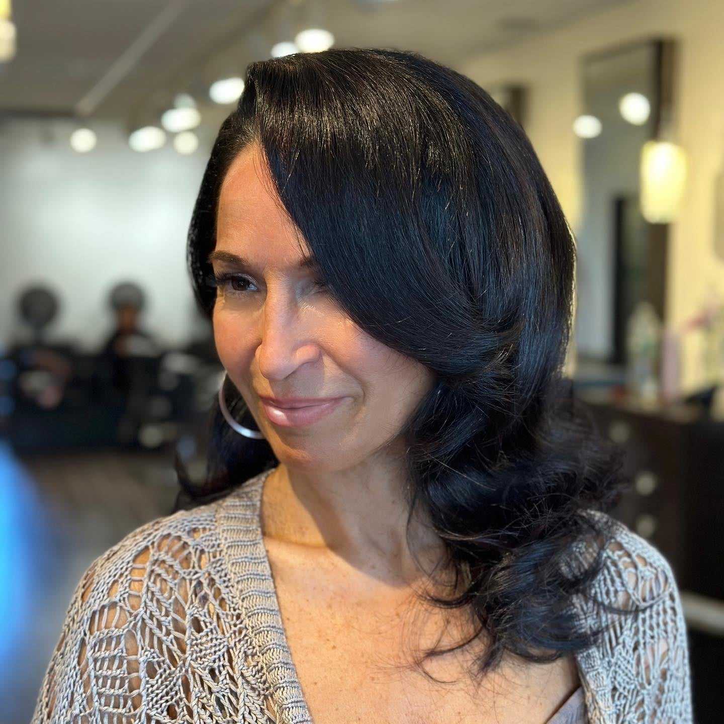 Elegant woman with long dark hair, smiling in a stylish salon setting.