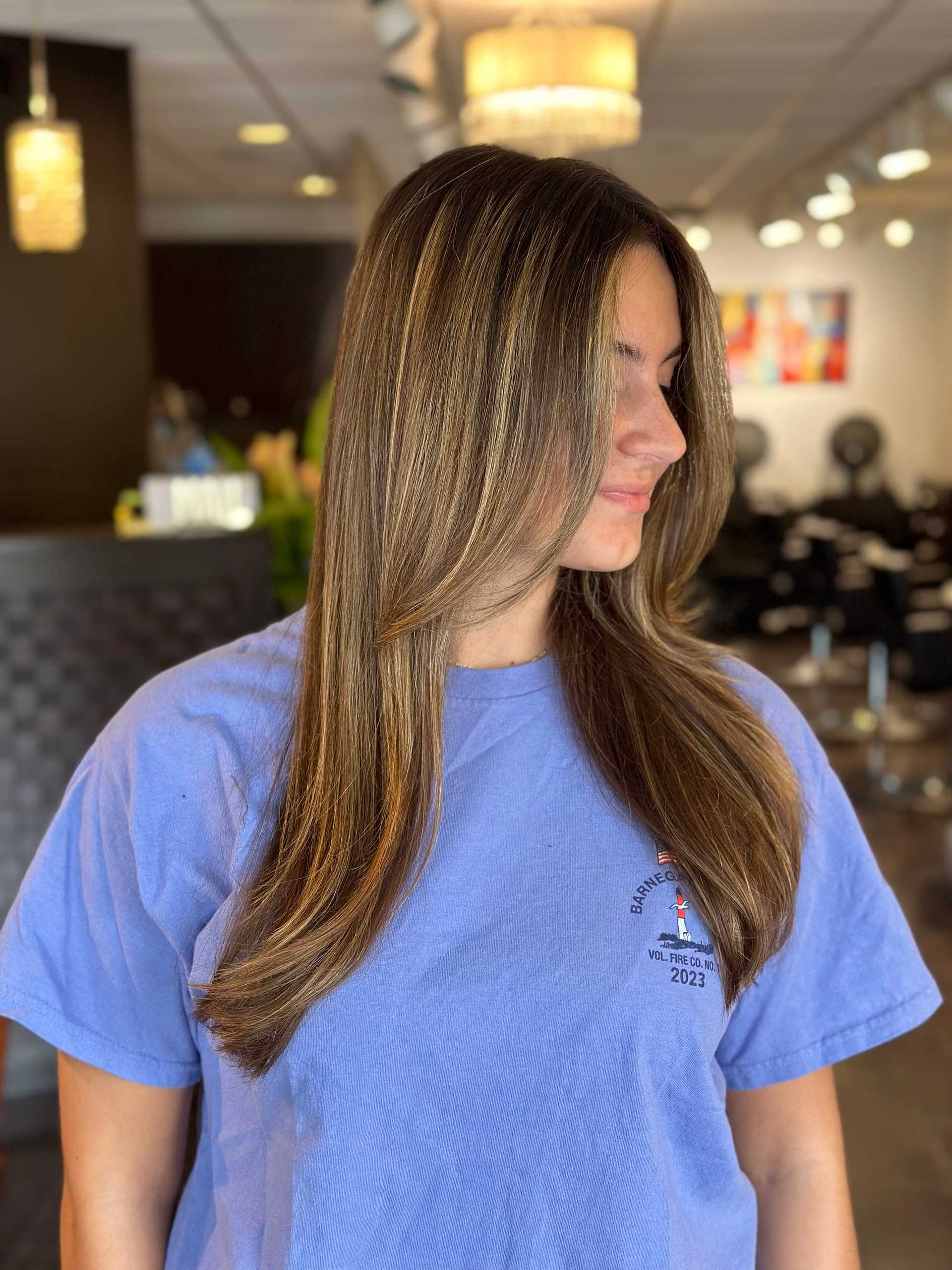 Woman with long highlighted hair in a salon, wearing a blue T-shirt.