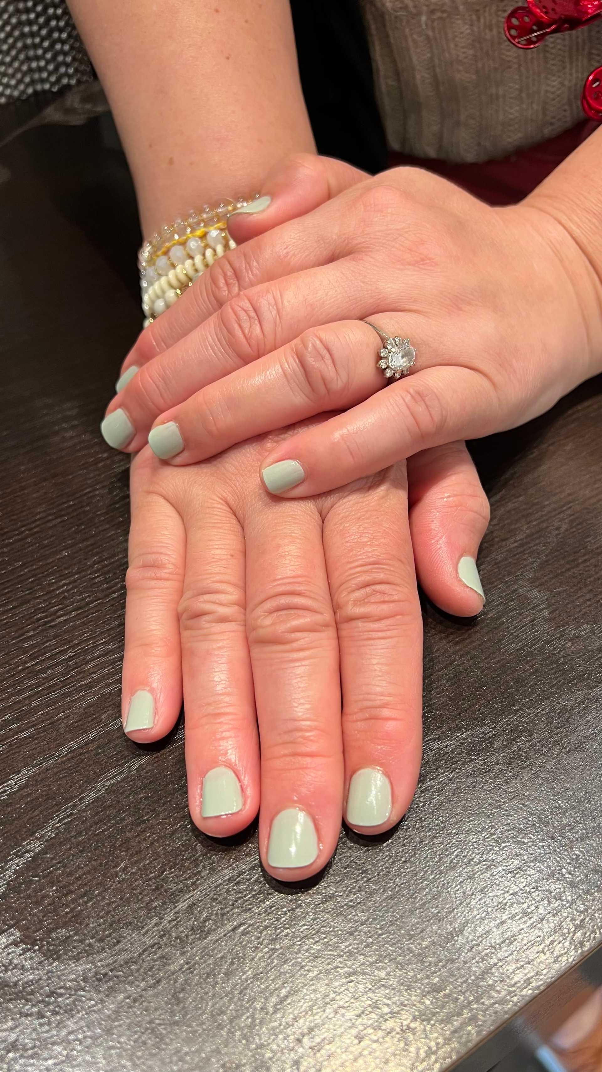 Hands with mint green nails and a diamond ring resting on a dark surface.